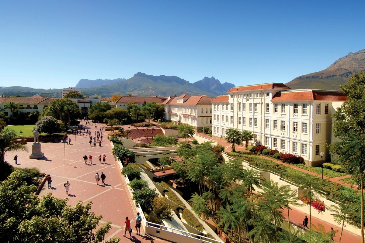 A landscaped green campus with paths, buildings, and mountains beyond.
