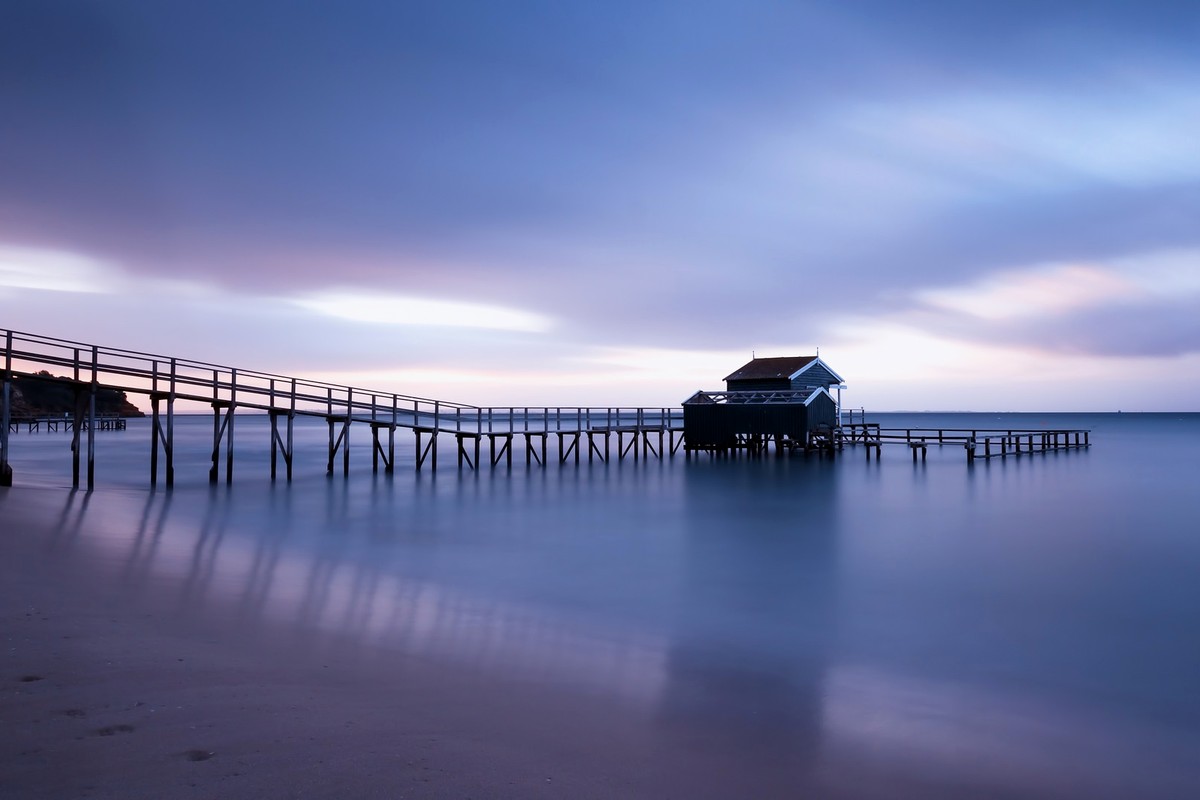 A long pier and calm water under a soft blue and violet evening sky.