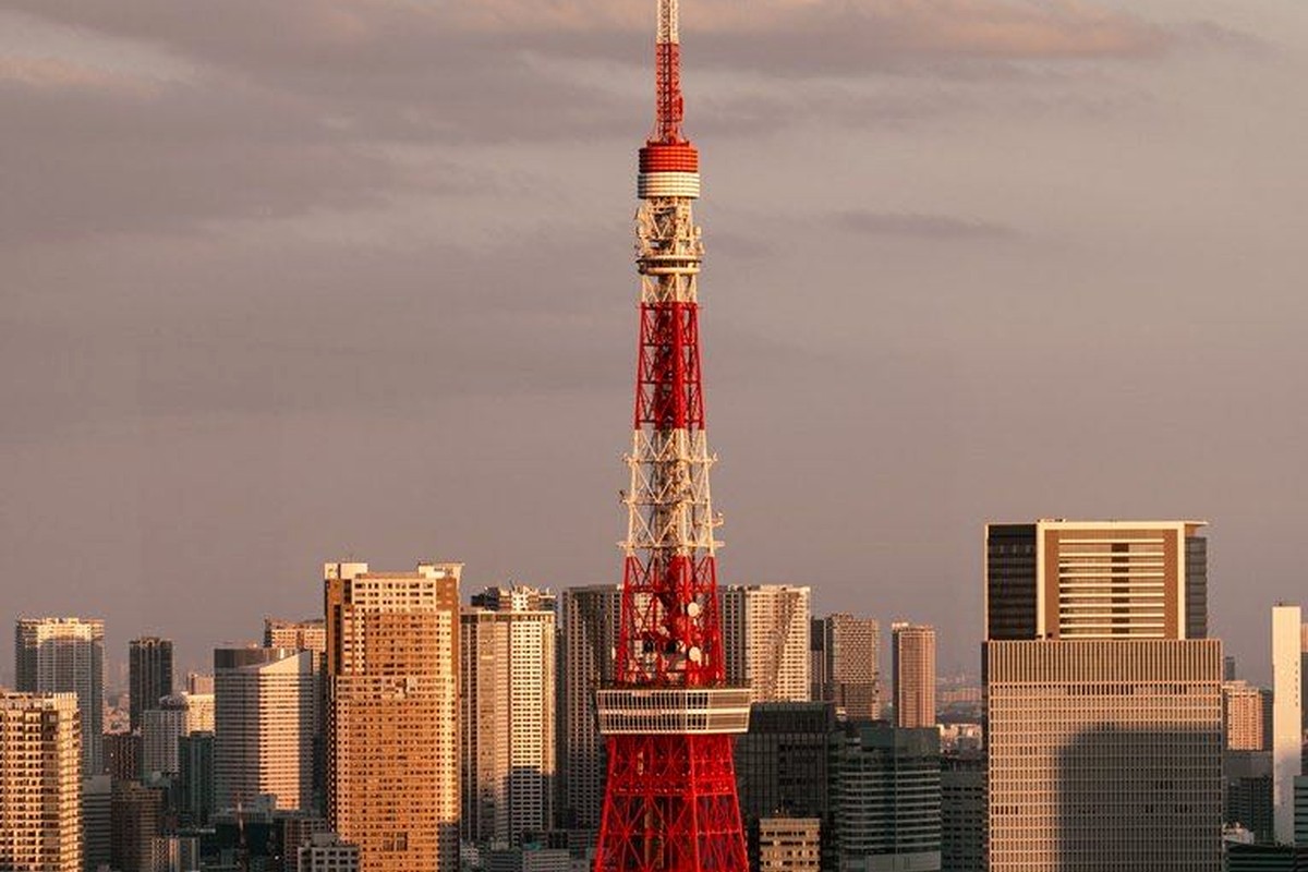 A red and white city tower rising above dense buildings in warm evening light.
